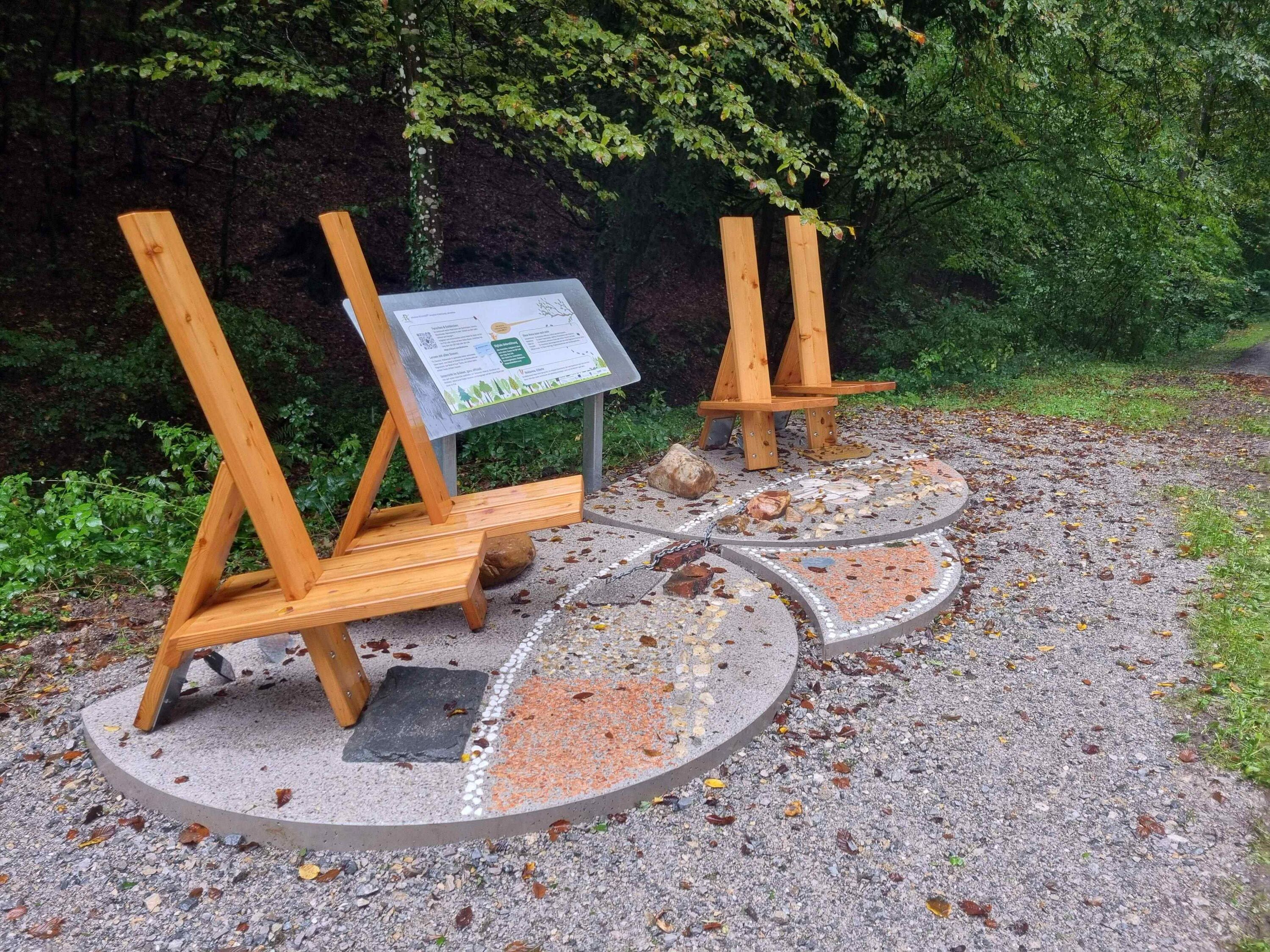 Das Bild zeigt vier Holzstühle vor denen im Boden unterschiedliche Materialien eingearbeitet sind, die mit den Füßen erfühlt werden können.