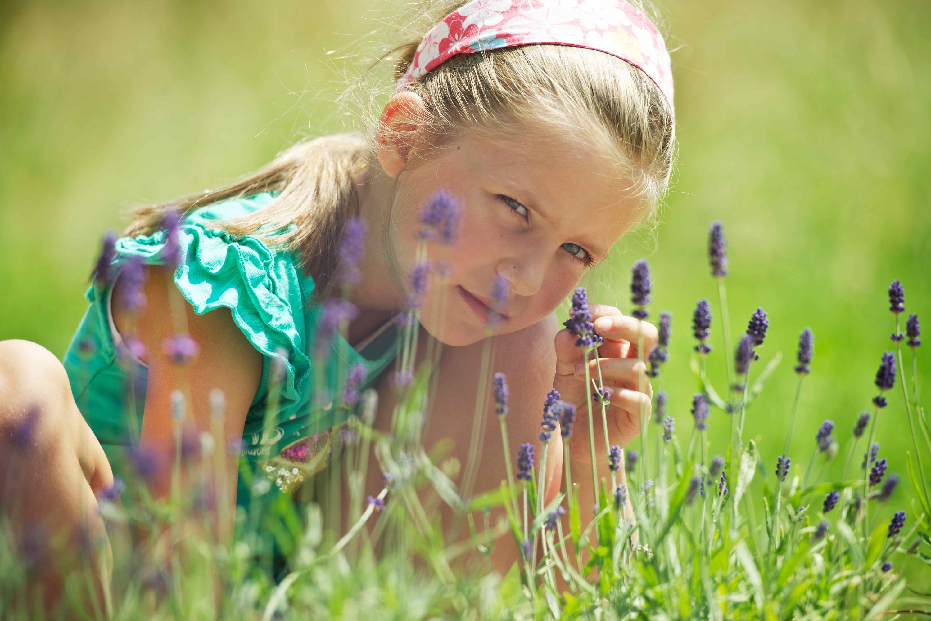 Bild zeigt die Erlebnisstation 17: Mädchen das in einer Blumenwiese sitzt und keck in die Kamera schaut.