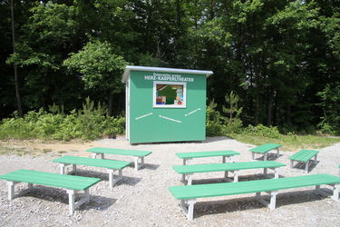 Station 9: Herz Kasperltheater Bild zeigt die Erlebnisstation 9: Kasperltheater in lebensgroßer grüner Box mit Sitzreihen davor.